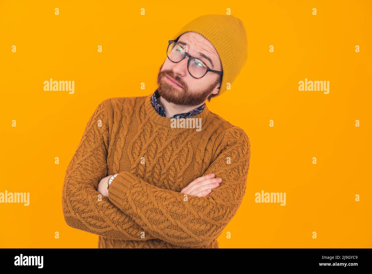 Il est temps de réfléchir. Dude caucasien barbu en pull avec bras croisés et visage de rêve sur fond jaune. Photo de haute qualité Banque D'Images