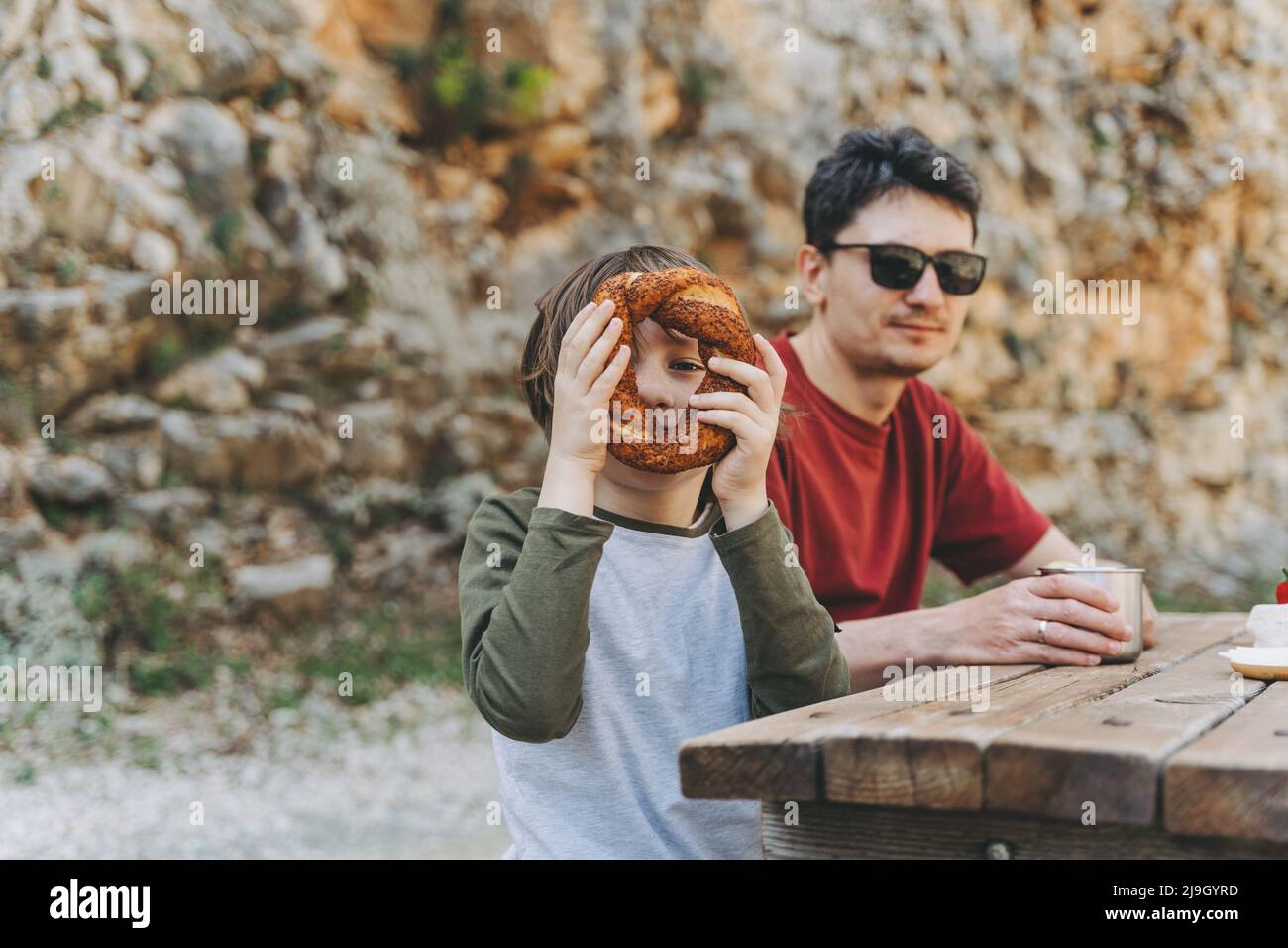 Garçon d'école enfant enfant heureux regardant à travers le pain de beignet tout en ayant un pique-nique en famille dans les montagnes avec son père papa Banque D'Images