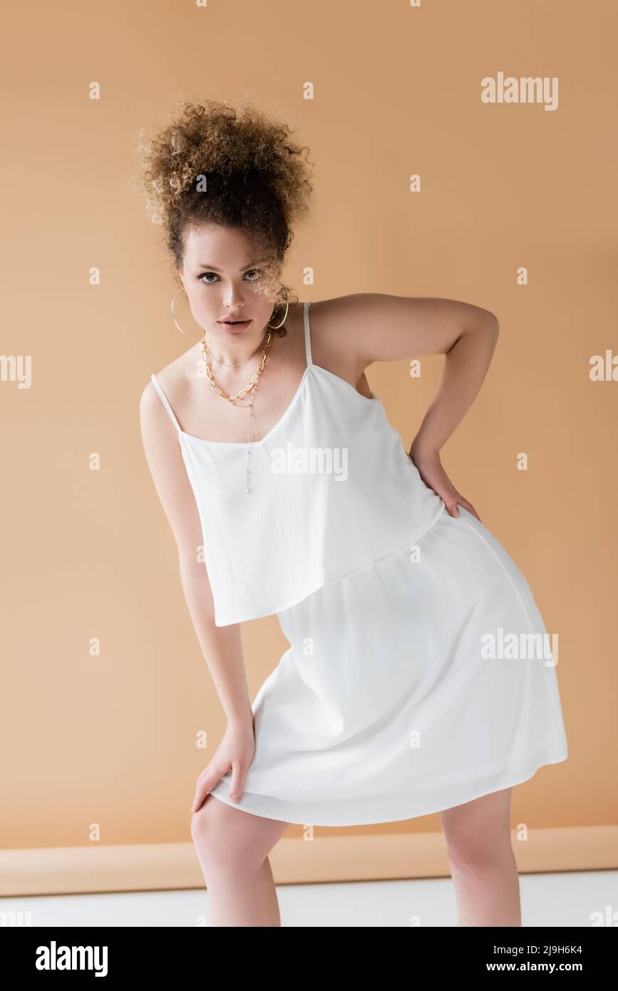 Femme élégante vêtue de vêtements blancs tenant la main sur la hanche sur fond beige Banque D'Images