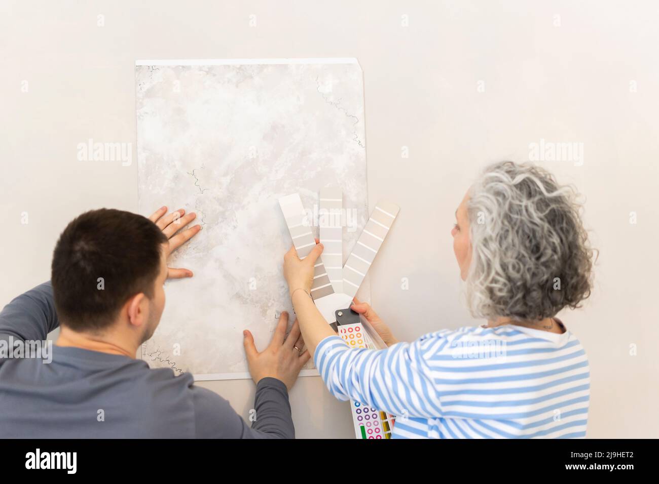 Une femme et un ami choisissent un papier peint et un catalogue de couleurs sur un mur Banque D'Images