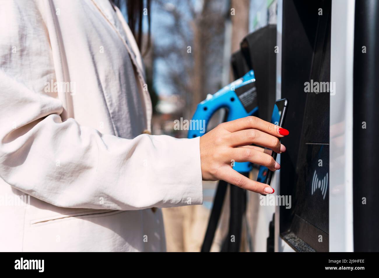 Femme effectuant un paiement sans contact par téléphone intelligent à la station de charge Banque D'Images