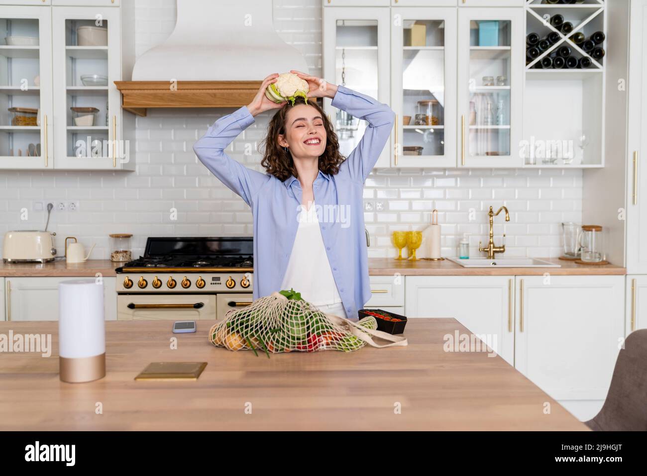 Femme souriante tenant le chou-fleur sur la tête dans la cuisine Banque D'Images