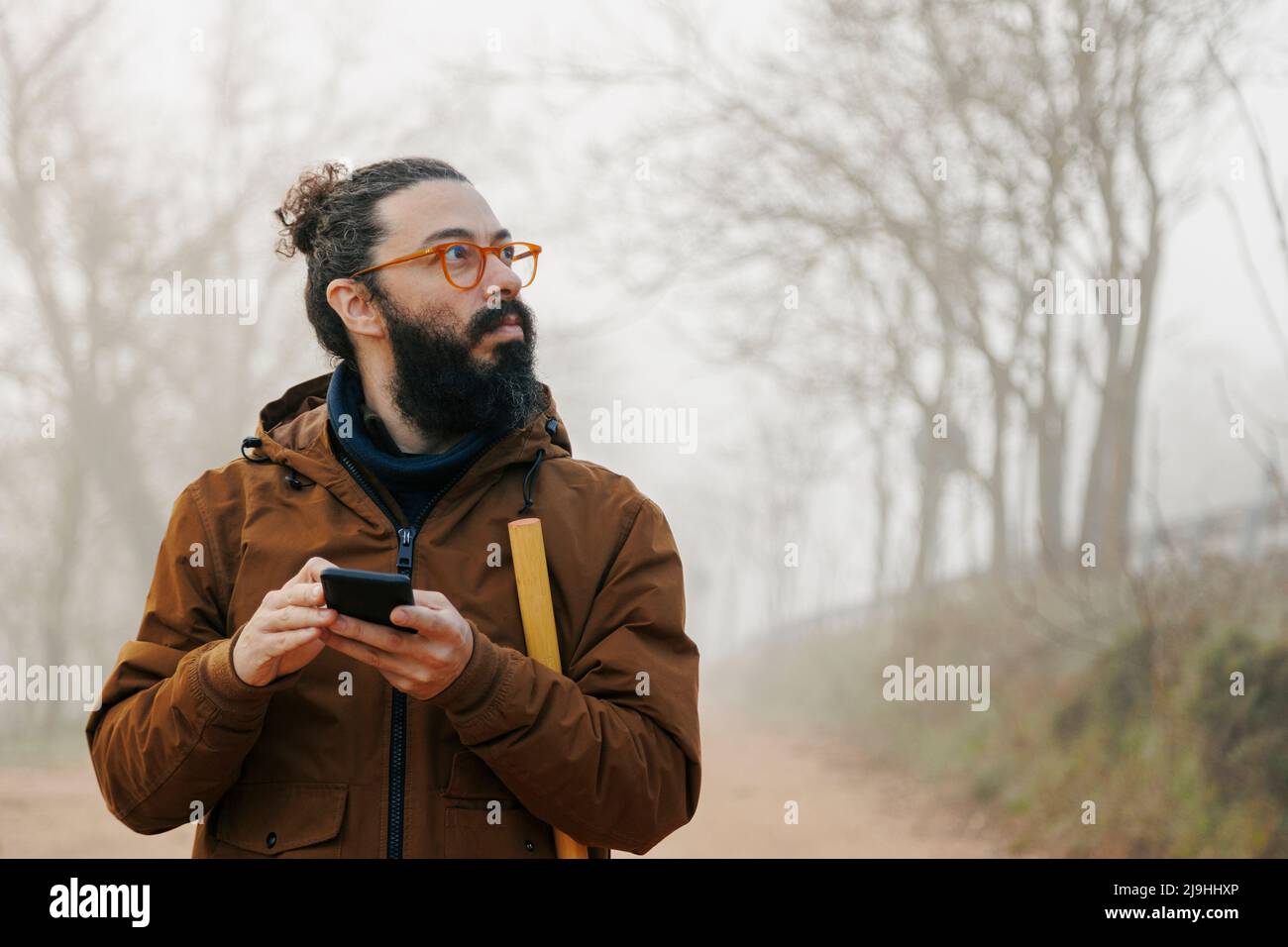 Homme mature portant des lunettes tenant un smartphone perdu dans la forêt Banque D'Images