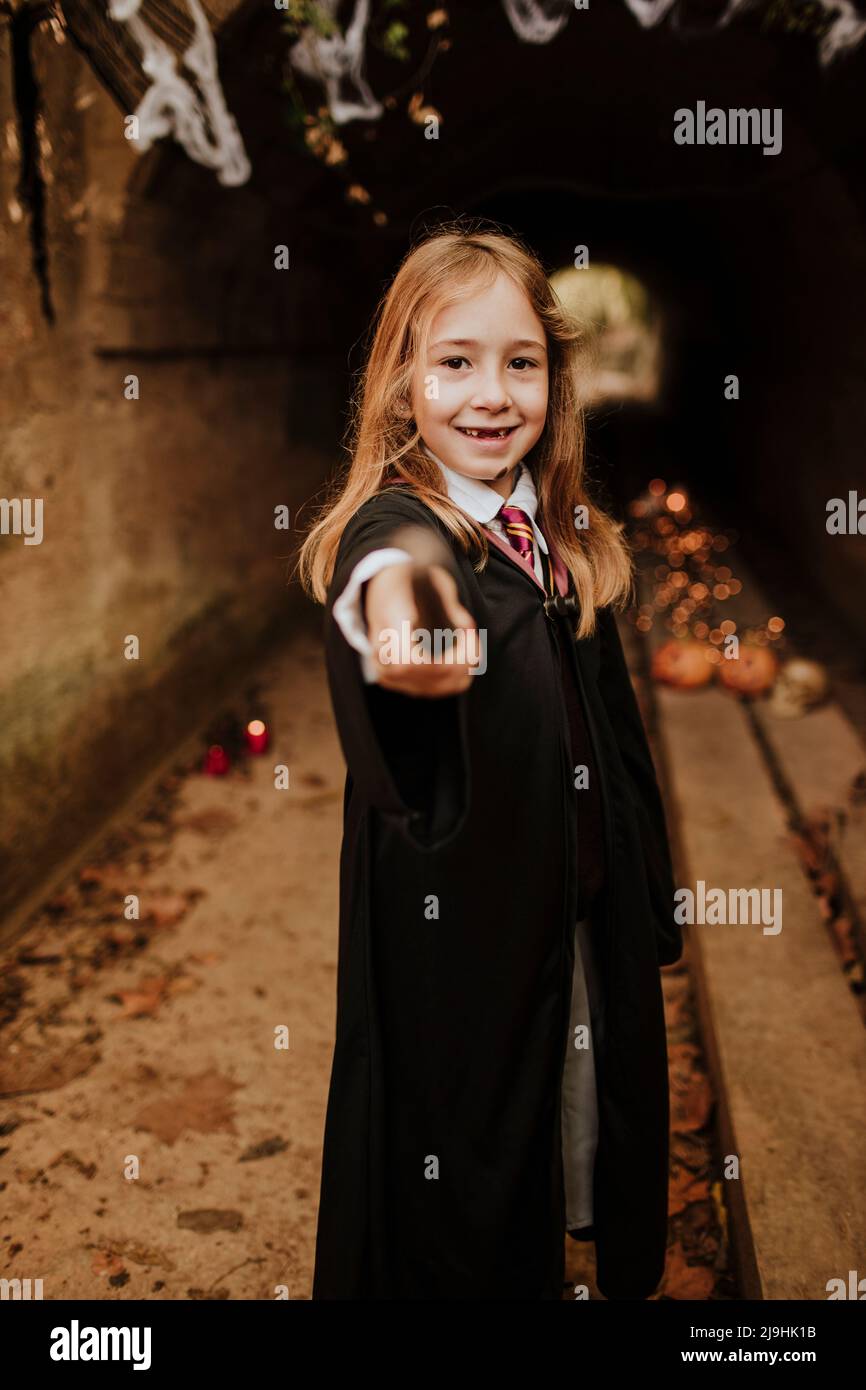 Fille souriante avec baguette magique portant un costume debout devant le tunnel Banque D'Images