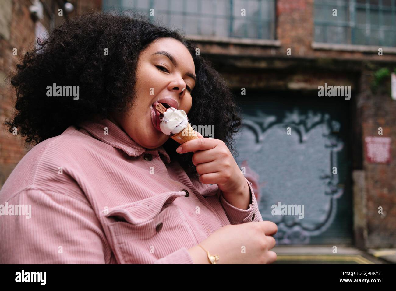 Jeune femme aux cheveux bouclés qui mange de la crème glacée Banque D'Images