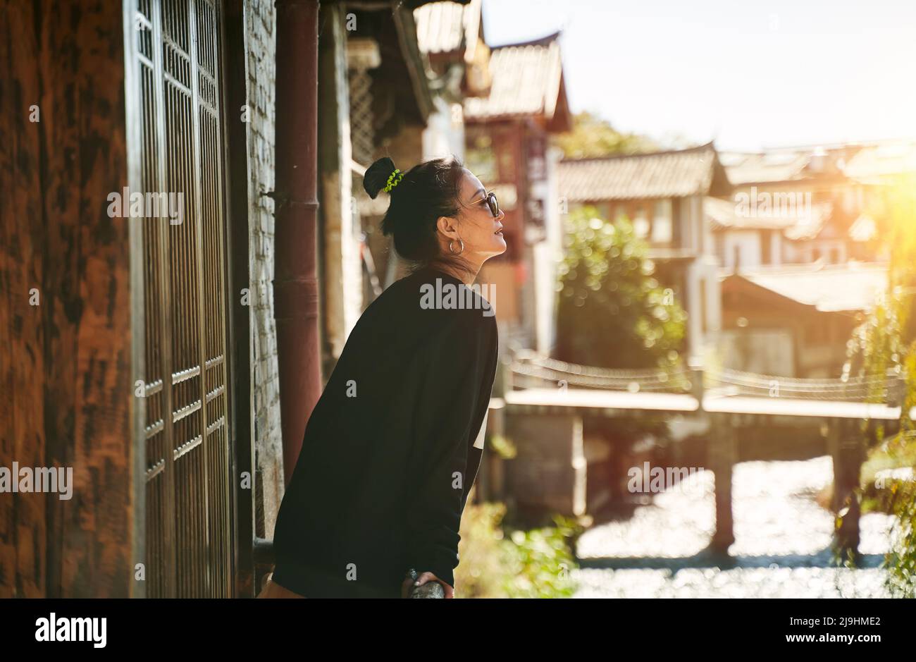 femme asiatique se détendant et profitant de la lumière du soleil à l'extérieur d'une maison traditionnelle en bois Banque D'Images