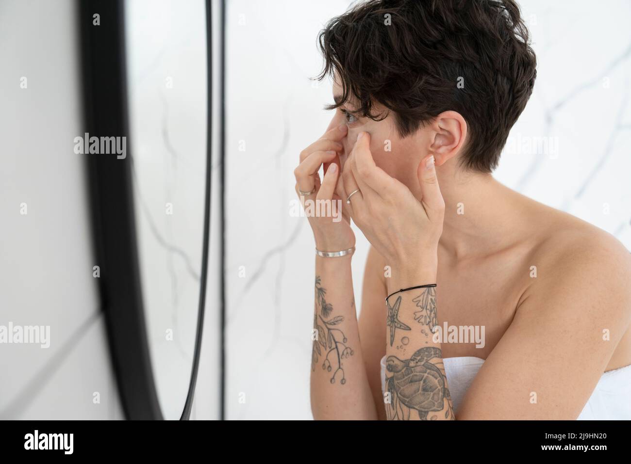 Femme appliquant un masque oculaire regardant le miroir dans la salle de bains Banque D'Images
