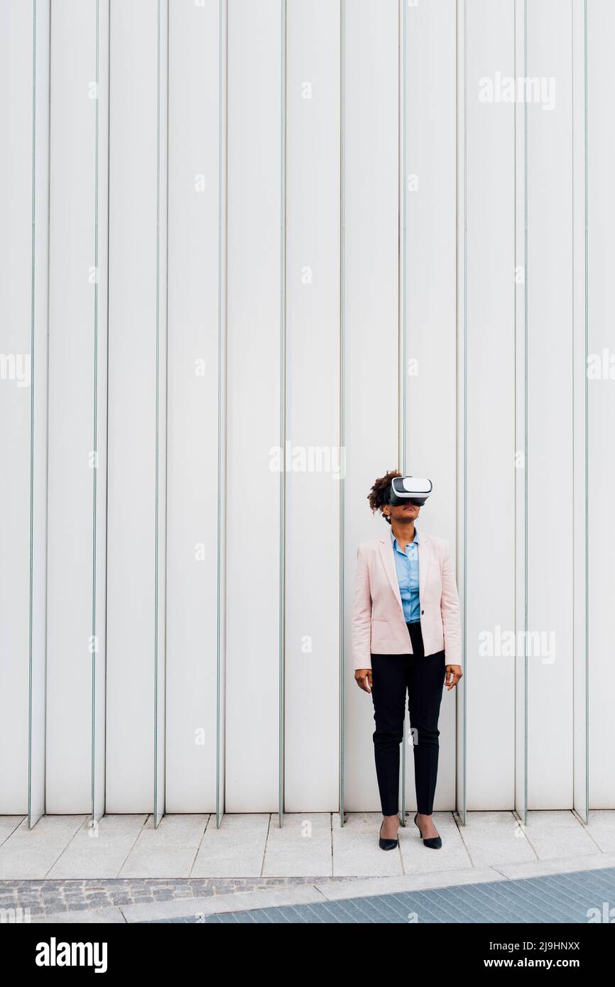 Femme d'affaires portant un simulateur de réalité virtuelle devant un mur blanc Banque D'Images