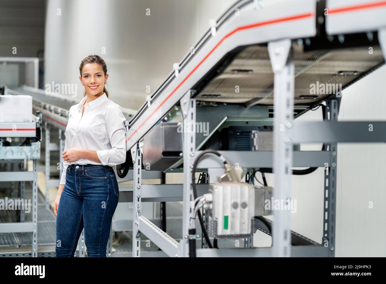 Femme d'affaires souriante debout près du tapis roulant en usine Banque D'Images