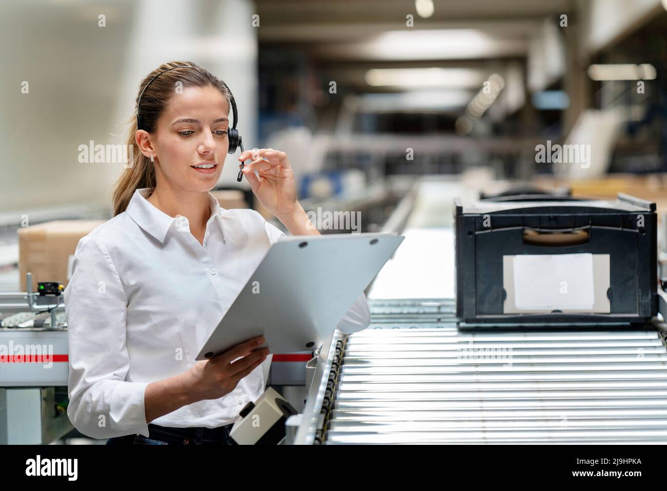 Jeune femme d'affaires lisant sur un presse-papiers avec un micro-casque à l'usine Banque D'Images