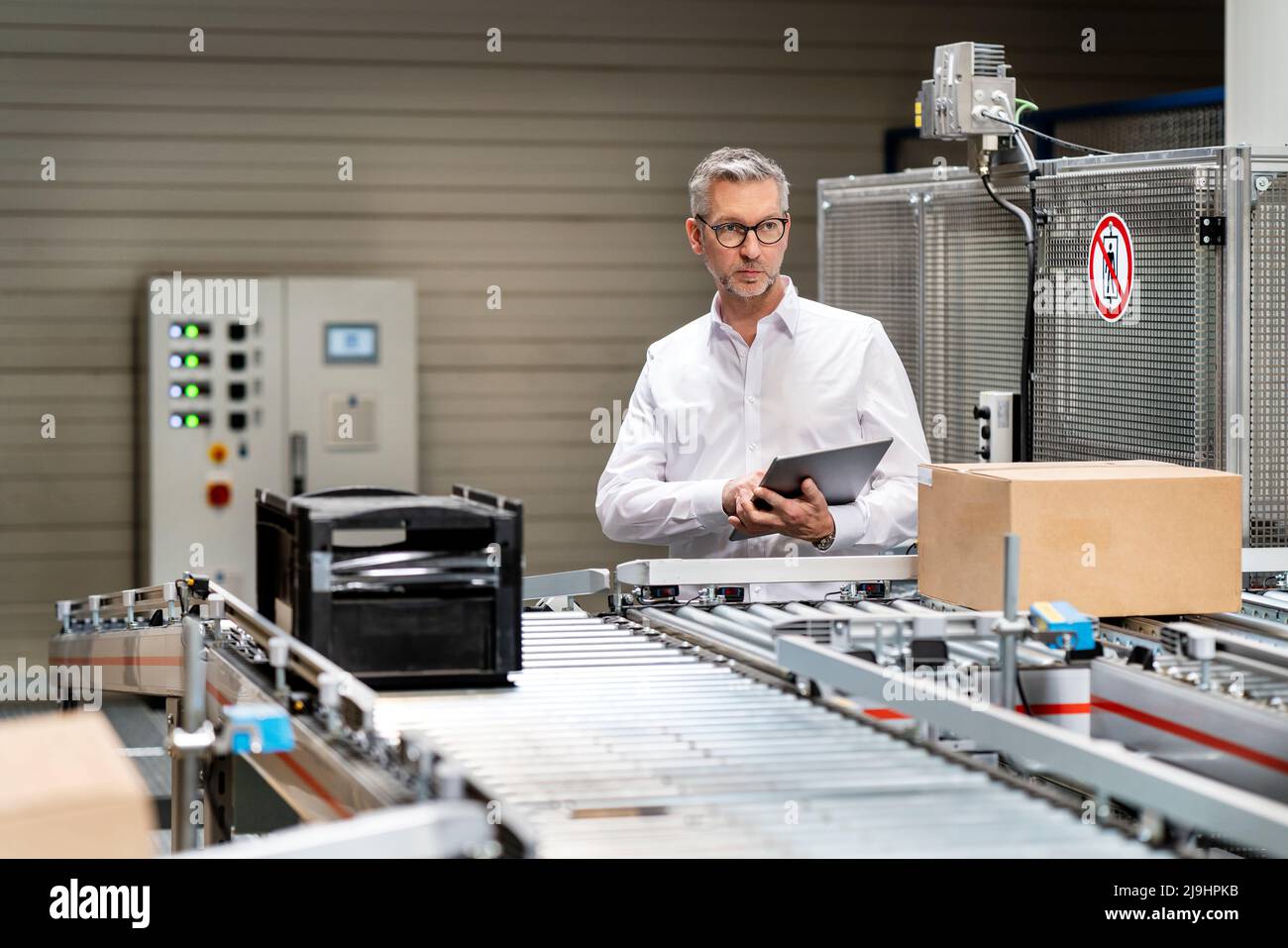 Homme d'affaires mature examinant une boîte sur un tapis convoyeur avec un Tablet PC en usine Banque D'Images