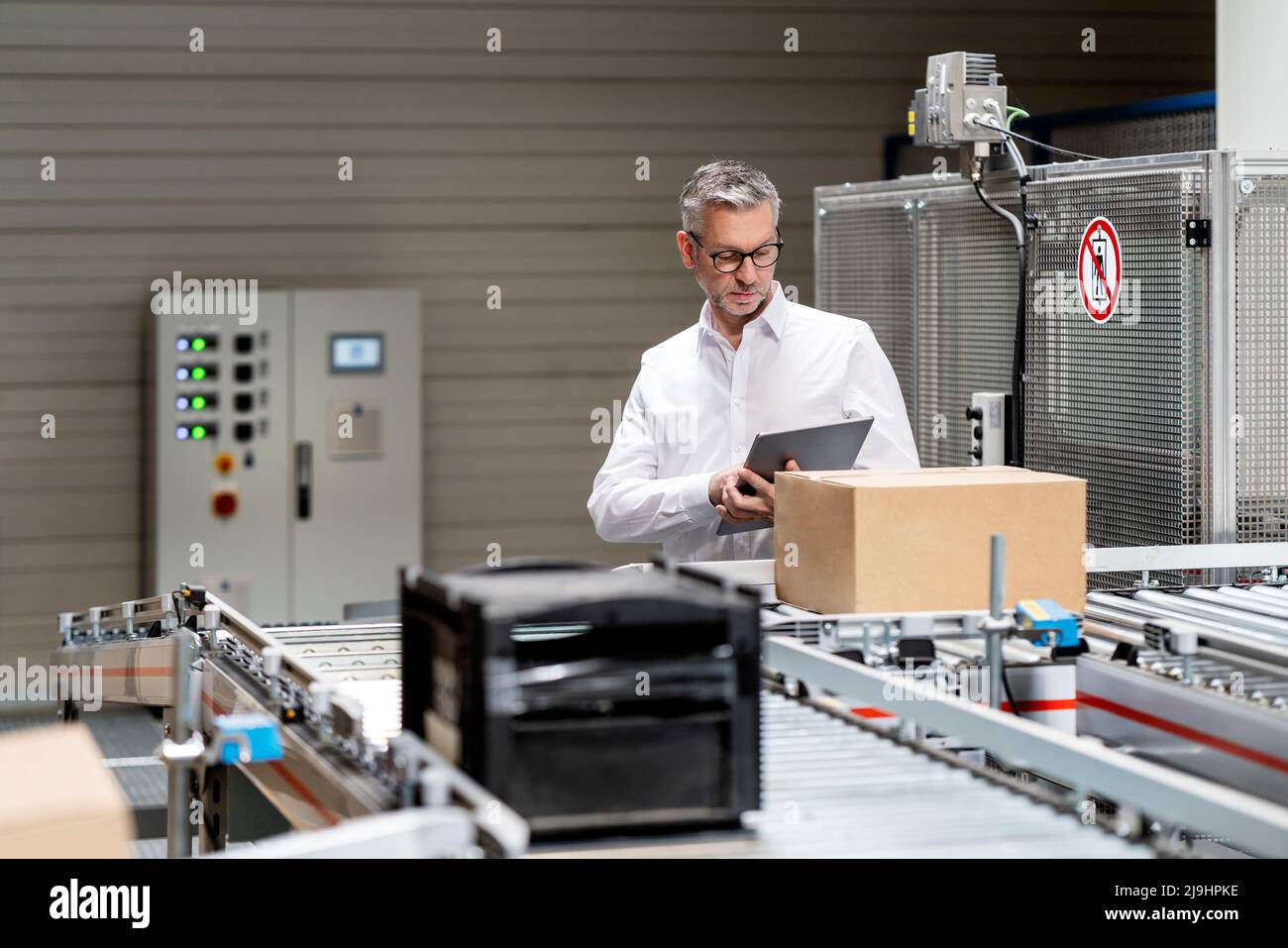 Homme d'affaires utilisant une tablette informatique par un tapis transporteur dans l'entrepôt Banque D'Images