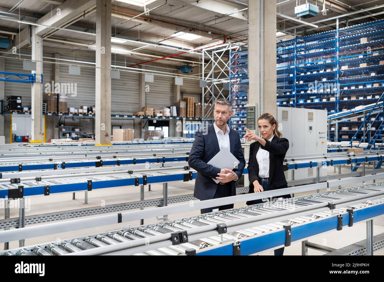 Jeune femme d'affaires discutant avec un collègue par tapis convoyeur en usine Banque D'Images