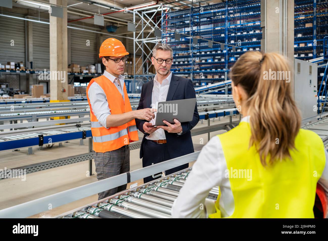 Un responsable mûr discute avec un collègue au sujet d'un ordinateur portable en usine Banque D'Images