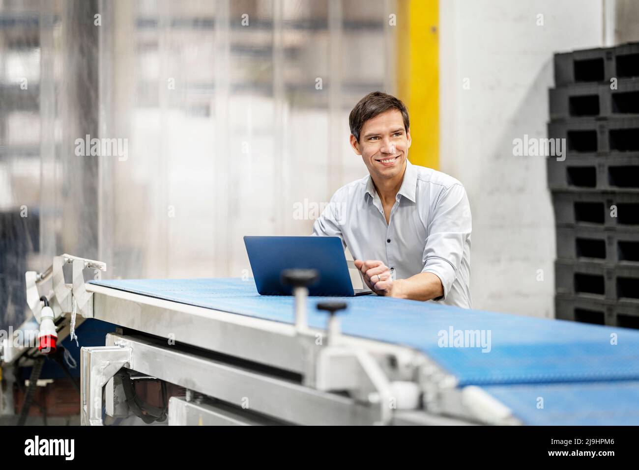 Homme d'affaires souriant avec un ordinateur portable sur le tapis transporteur dans l'entrepôt Banque D'Images