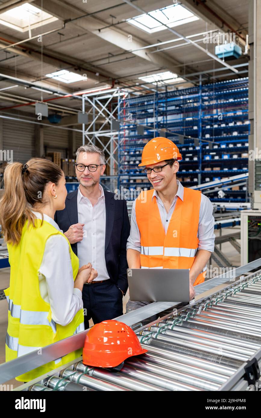 Jeune ouvrier de cols bleus discutant avec un homme d'affaires et un collègue dans l'entrepôt Banque D'Images