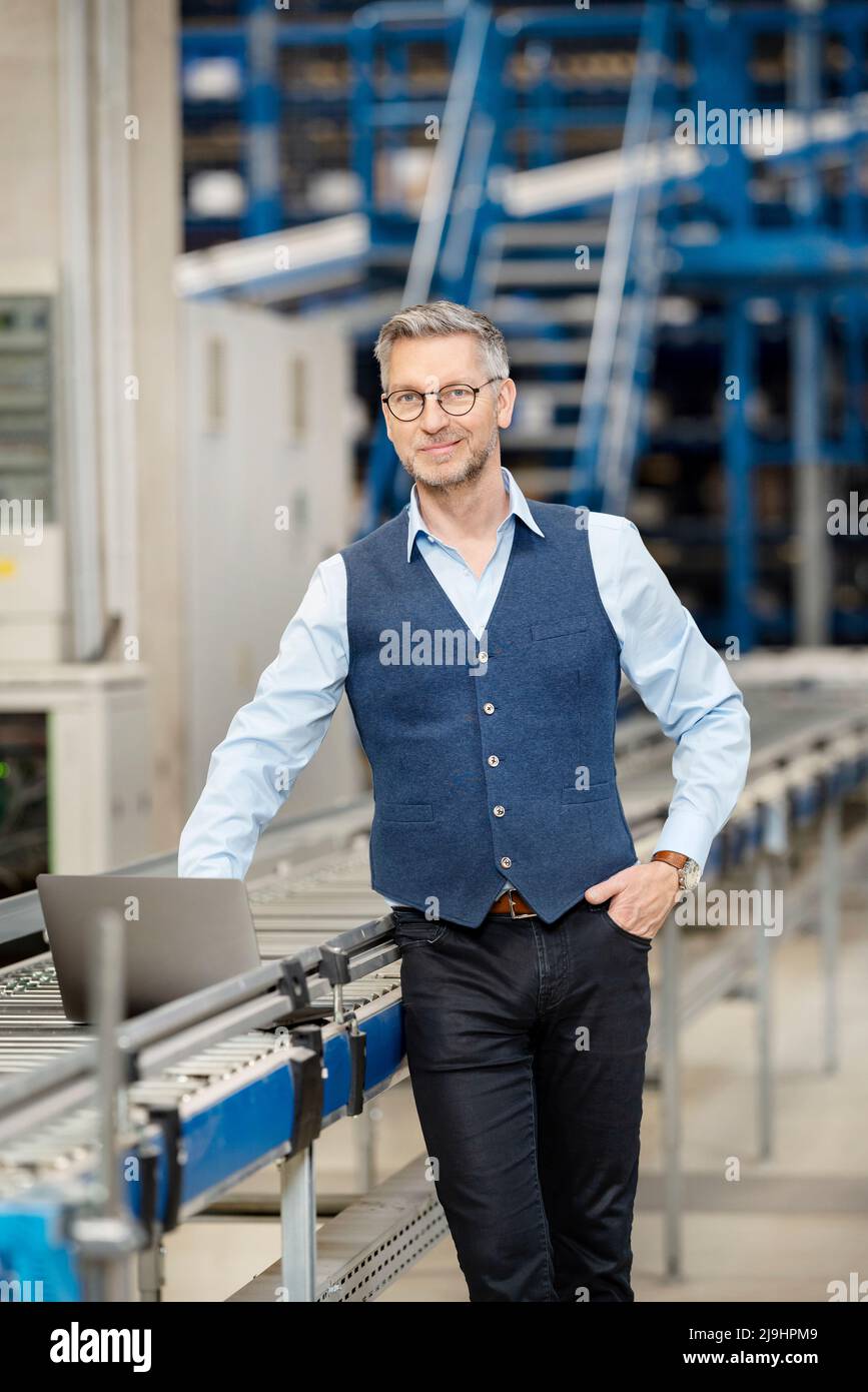Homme d'affaires souriant avec un ordinateur portable sur le tapis transporteur dans l'entrepôt Banque D'Images