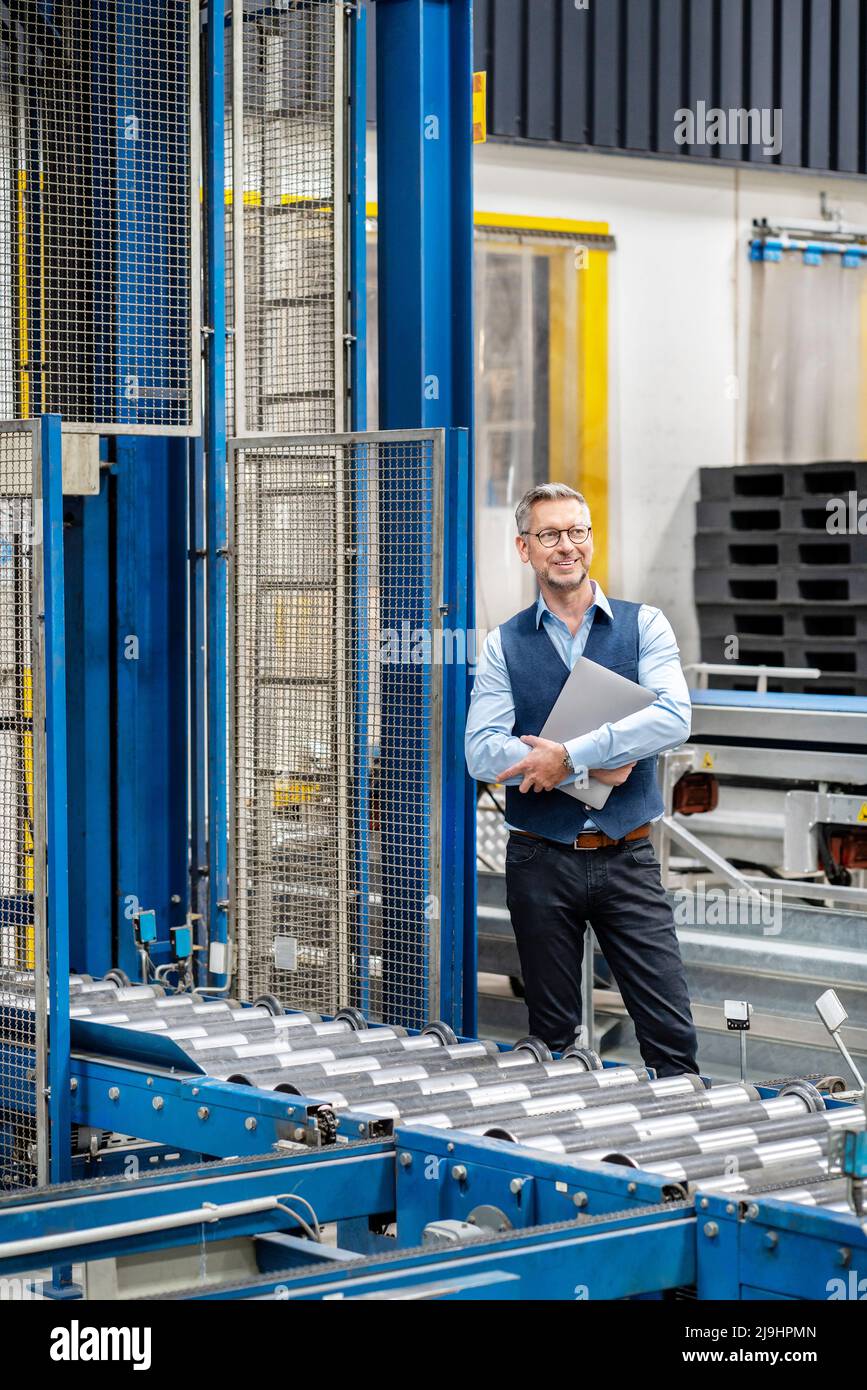 Homme d'affaires mature avec ordinateur portable debout à l'usine Banque D'Images