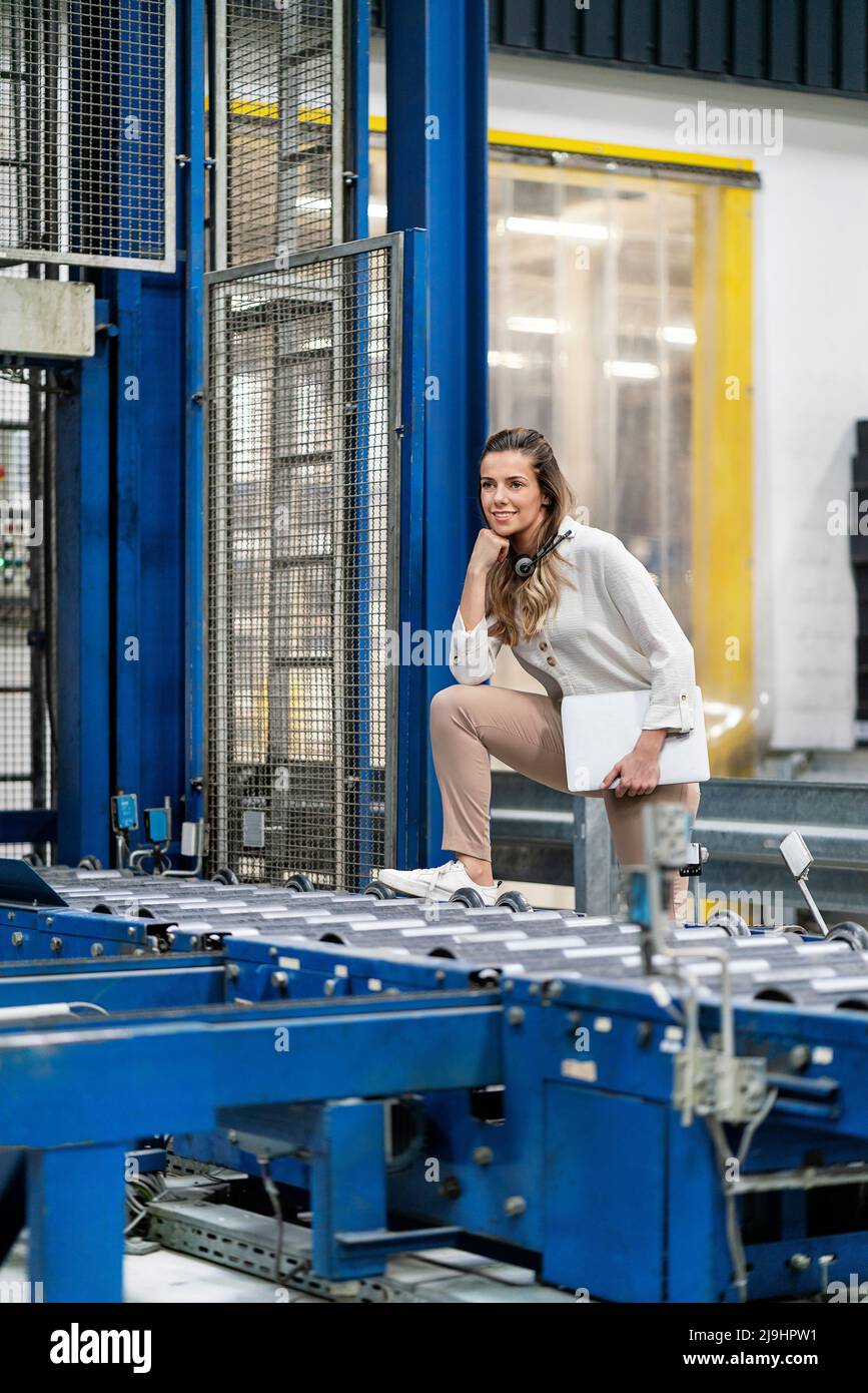 Jeune femme d'affaires avec une jambe sur un tapis roulant en usine Banque D'Images