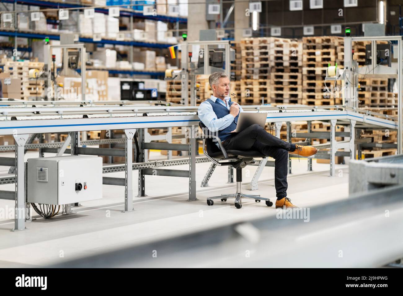 Homme d'affaires contemplatif assis sur une chaise dans l'usine Banque D'Images