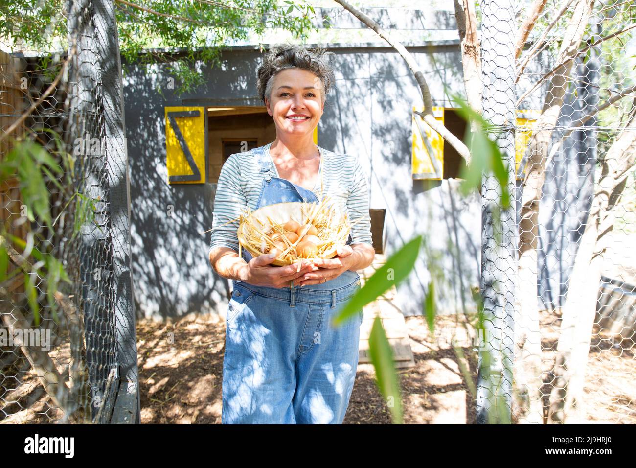 Joyeux fermier avec un bol d'oeufs debout à la ferme de volaille Banque D'Images