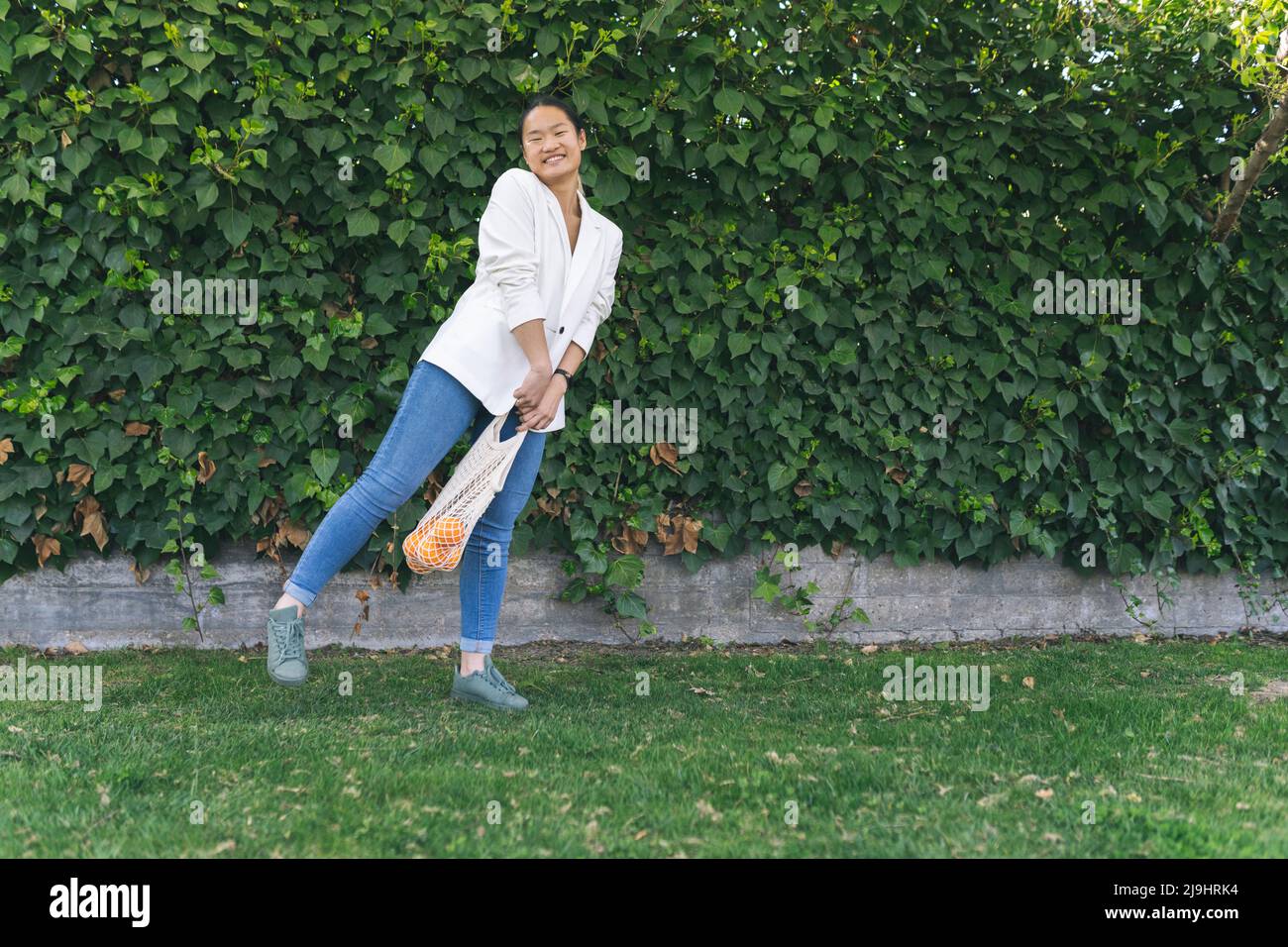 Bonne jeune femme tenant un sac en filet devant les plantes Banque D'Images