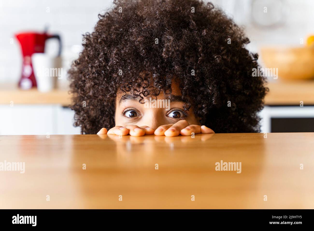 Femme avec la coiffure afro se cachant derrière l'île de cuisine à la maison Banque D'Images