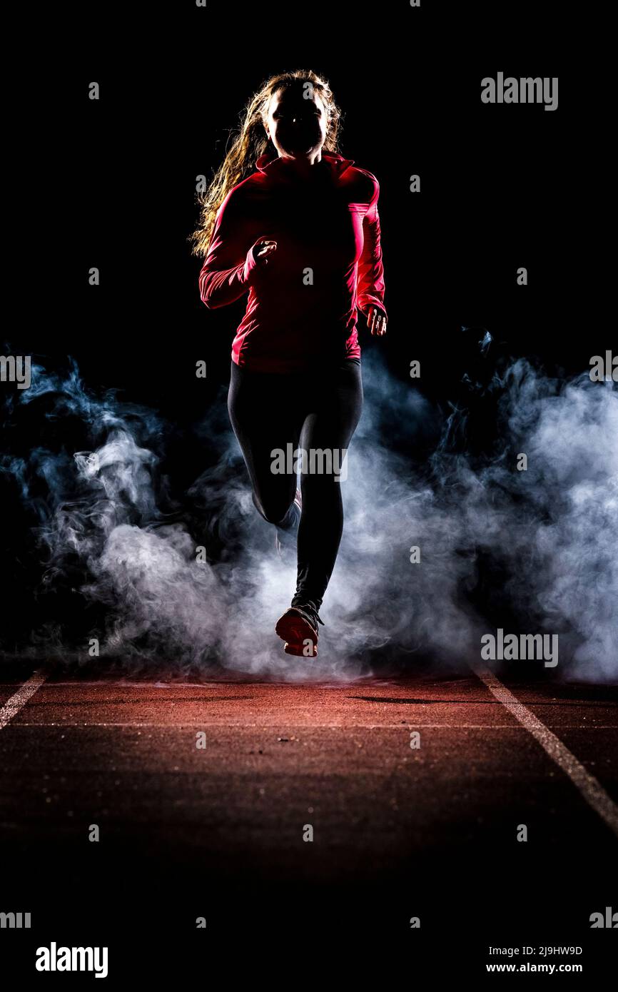 Jeune femme qui fait du jogging sur une piste de course dans la nuit, dans le brouillard Banque D'Images