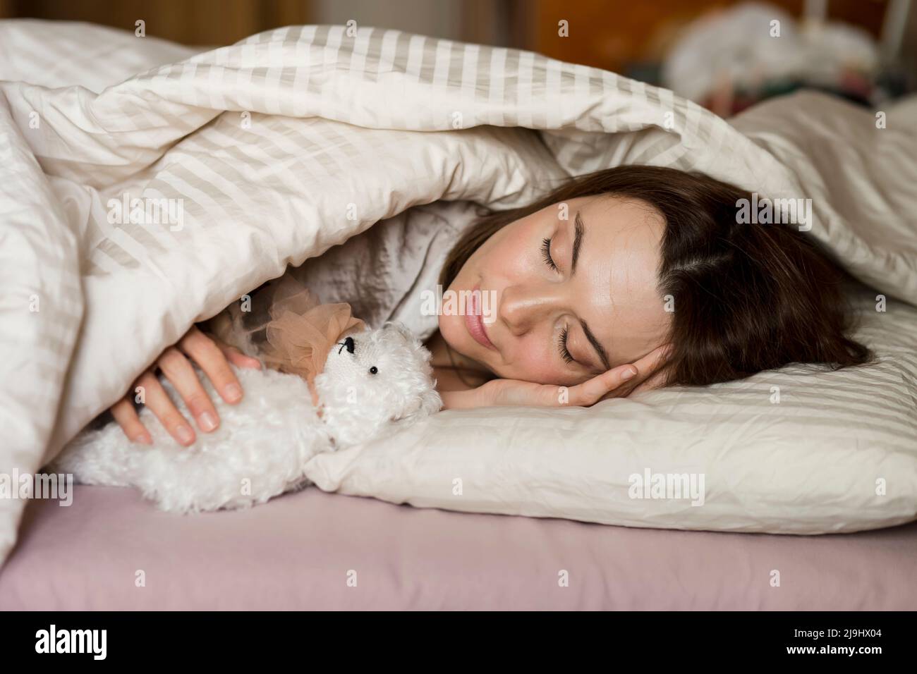 Femme adulte avec ours en peluche dormant sur le lit à la maison Banque D'Images