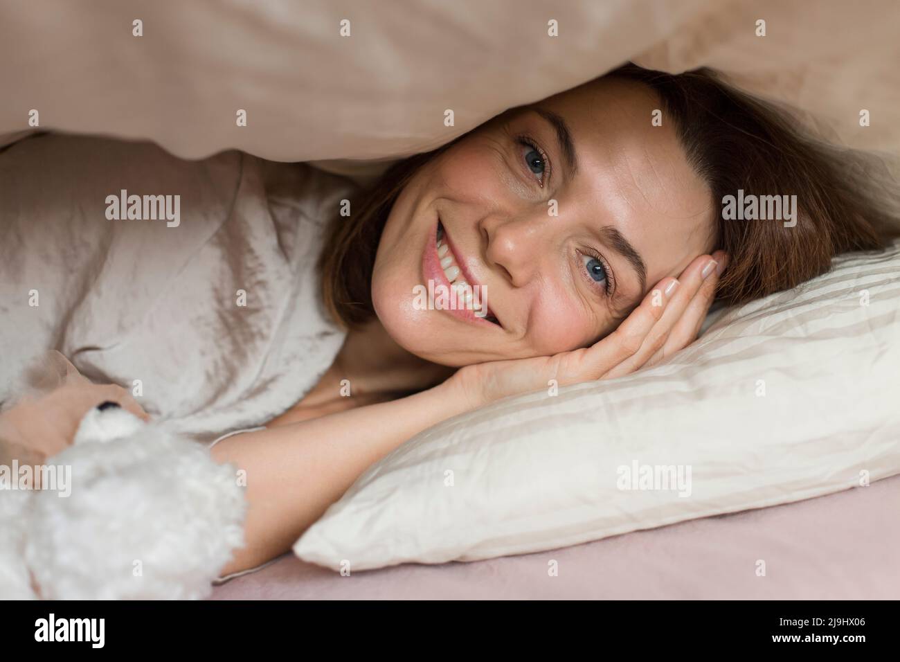 Bonne femme adulte avec jouet ours en peluche couché sous une couverture sur le lit à la maison Banque D'Images