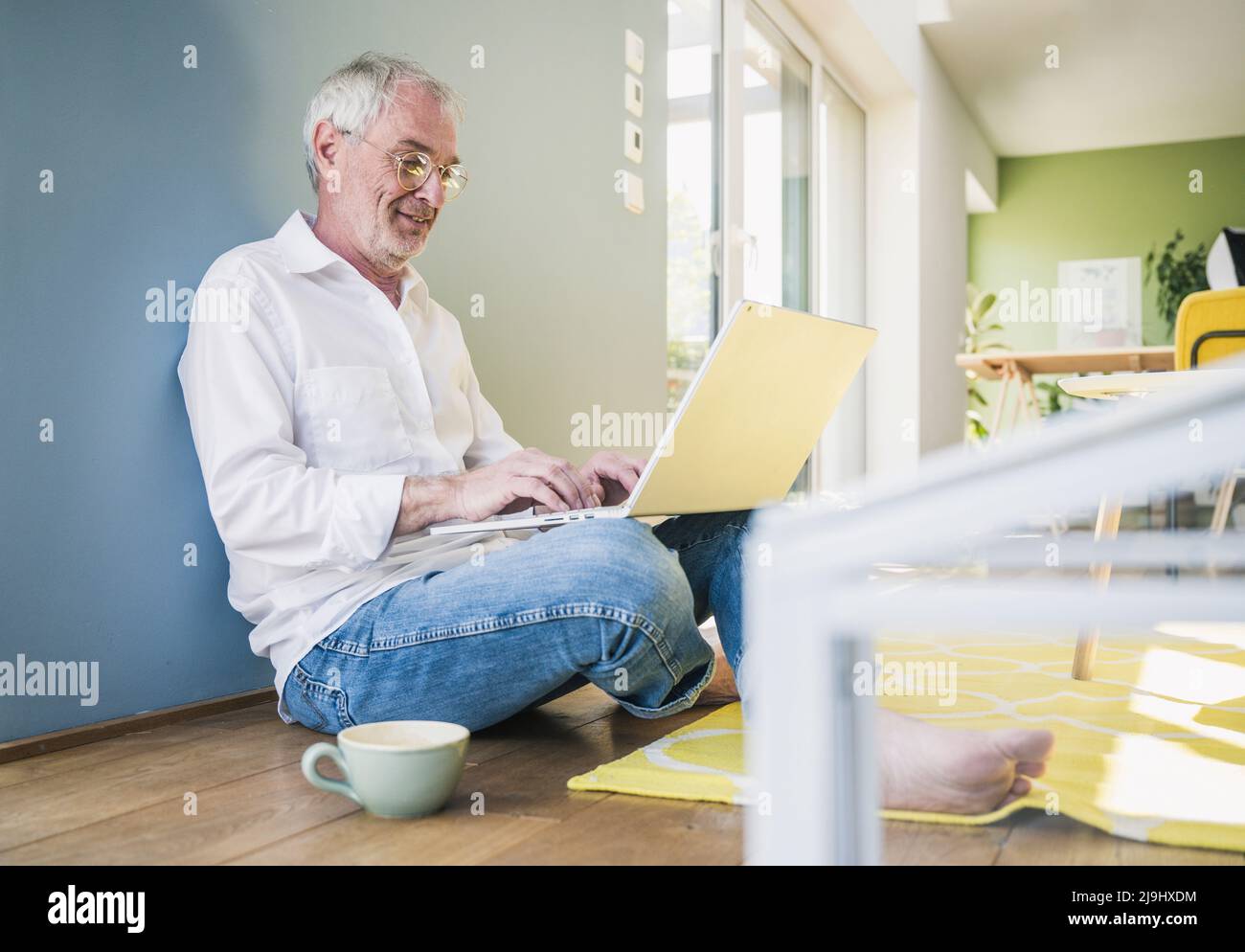 Homme senior souriant portant des lunettes à l'aide d'un ordinateur portable à la maison Banque D'Images