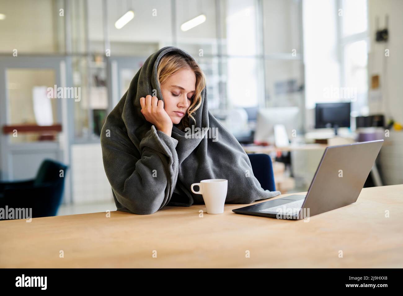 Une jeune femme fatiguée dans un confortable salon, assise au bureau avec ordinateur portable Banque D'Images