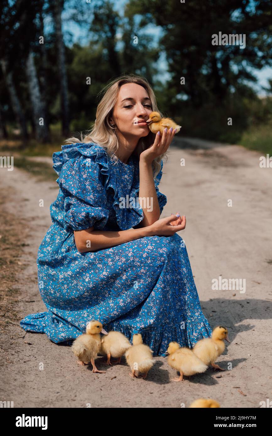 Belle jeune blonde dans une robe bleue dans les bois avec des ducklings Banque D'Images