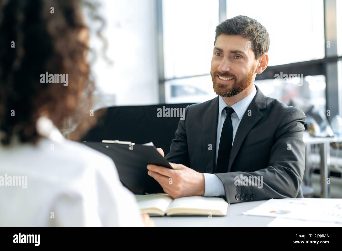 Homme de race blanche réussi, gestionnaire d'embauche dans une entreprise, conduit une entrevue avec une fille, dans un bureau moderne, examine le curriculum vitae du candidat, prend des notes, pose des questions, prend une décision Banque D'Images
