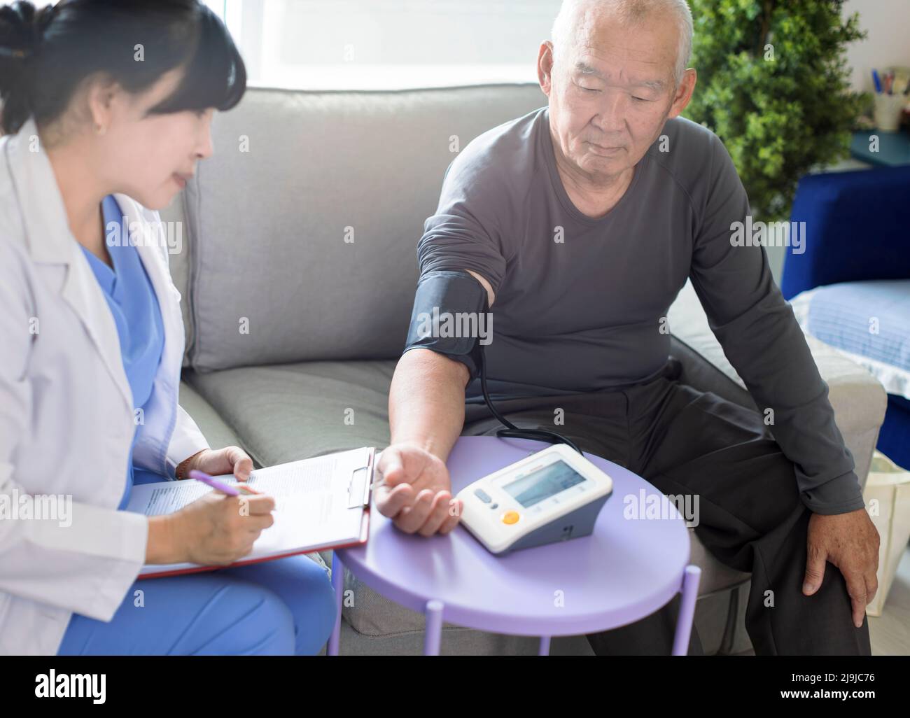 Un médecin soignant asiatique examine les patients âgés qui utilisent un manomètre de pression artérielle. Banque D'Images