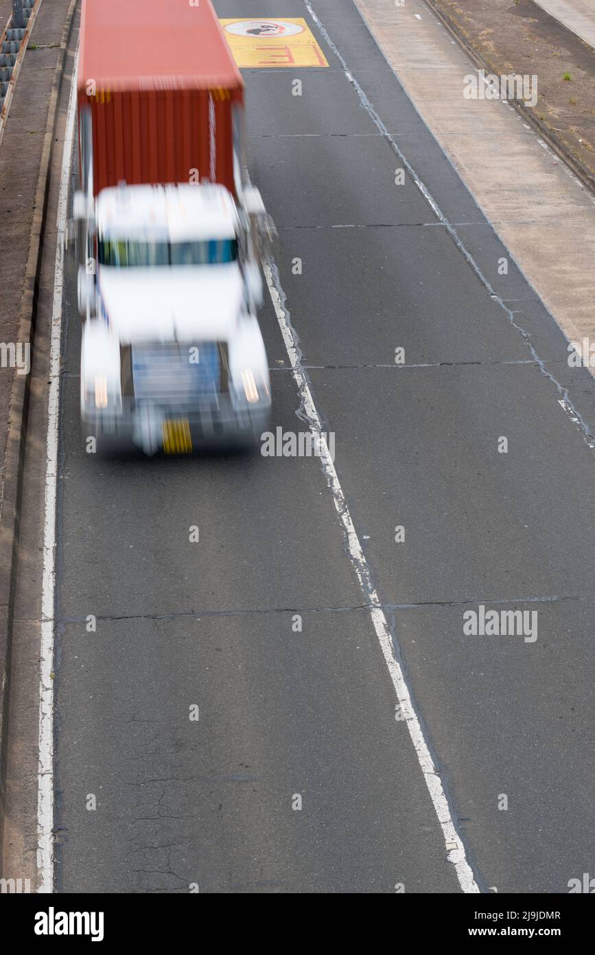 Image floue du dessus et devant un semi-remorque (pas de marque) transportant un conteneur d'expédition sur une autoroute à Sydney, en Australie Banque D'Images