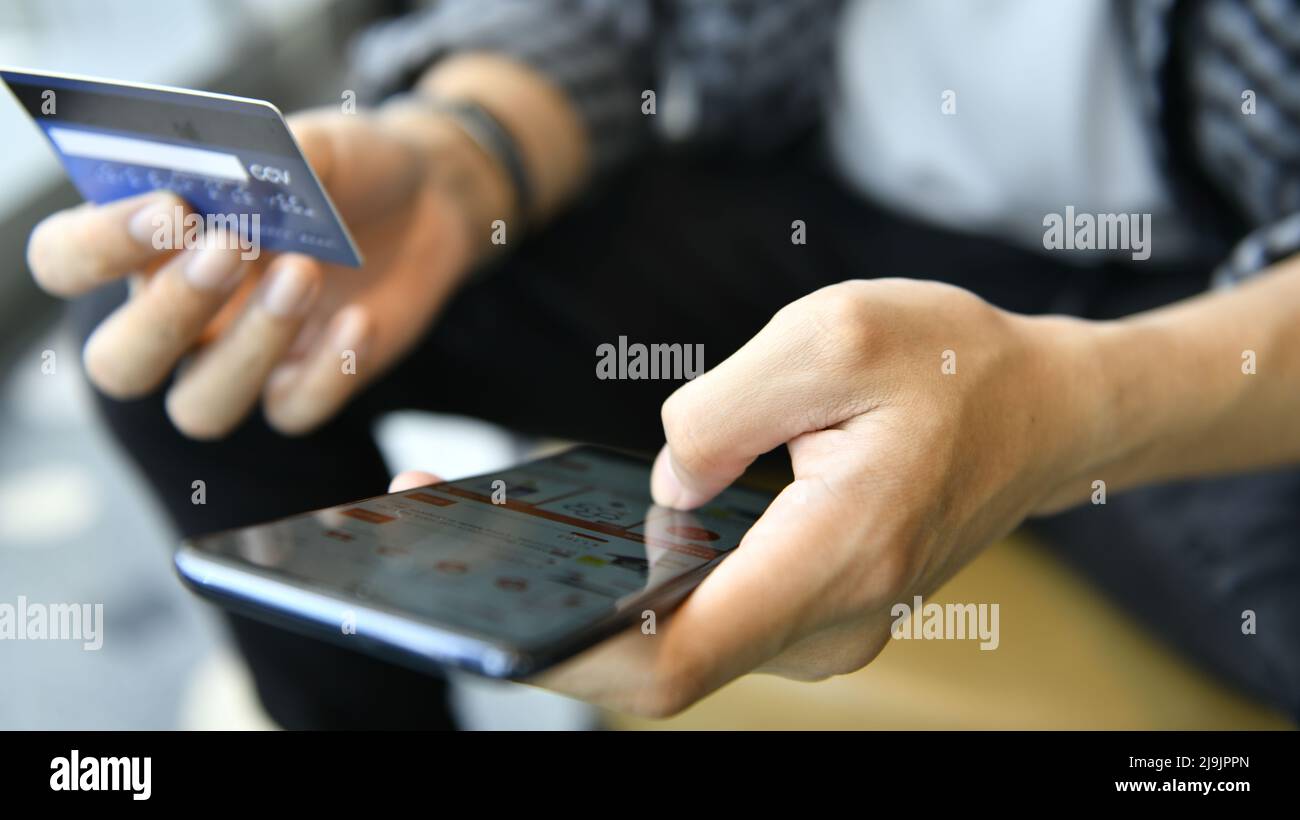 Mains tenant une carte de crédit et utilisant un smartphone pour faire des achats en ligne Banque D'Images