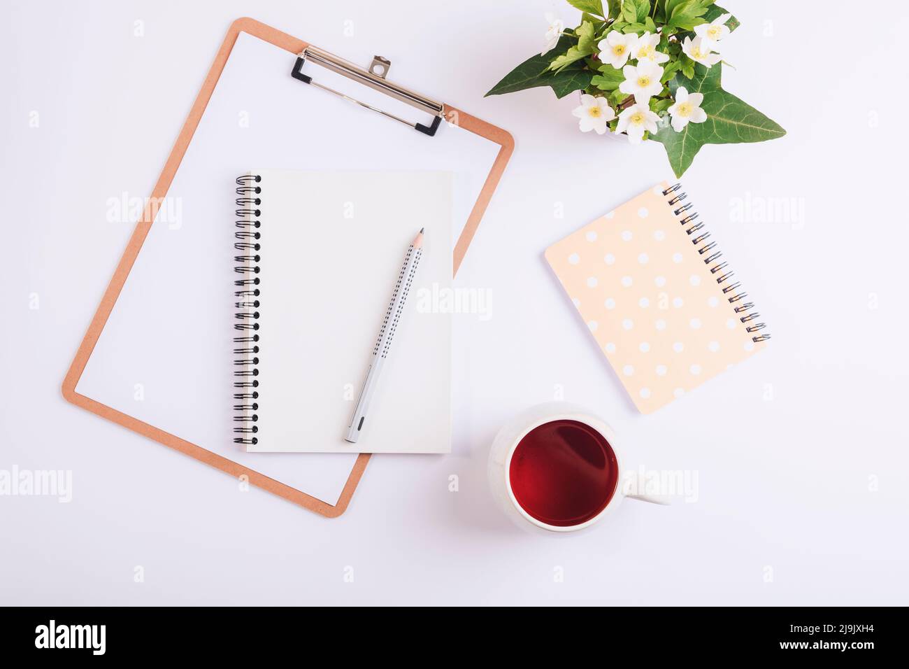 Bureau blanc avec presse-papiers, tasse de thé, crayon, carnet et bouquet de fleurs printanières. Flat lay, vue de dessus, maquette. Banque D'Images