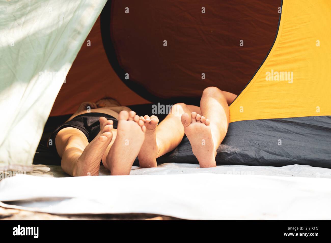 les pieds des enfants sortent d'une tente campant dans les bois au soleil, les pieds des enfants dans un bâton, camping Banque D'Images