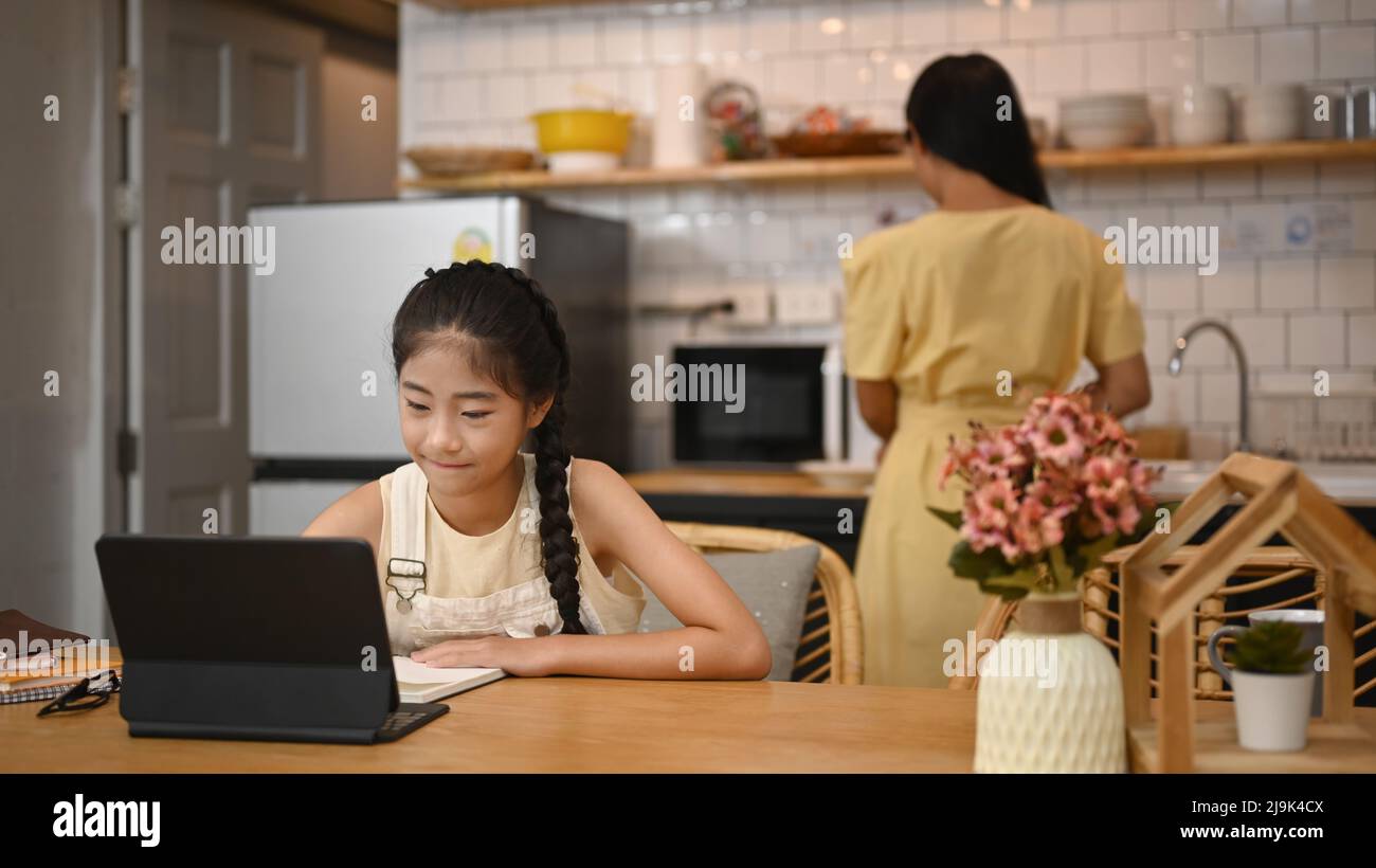 Focalisé petite fille asiatique regardant la leçon vidéo sur ordinateur portable, intéressé par le Web virtuel en ligne classe étudiant à la maison. Banque D'Images