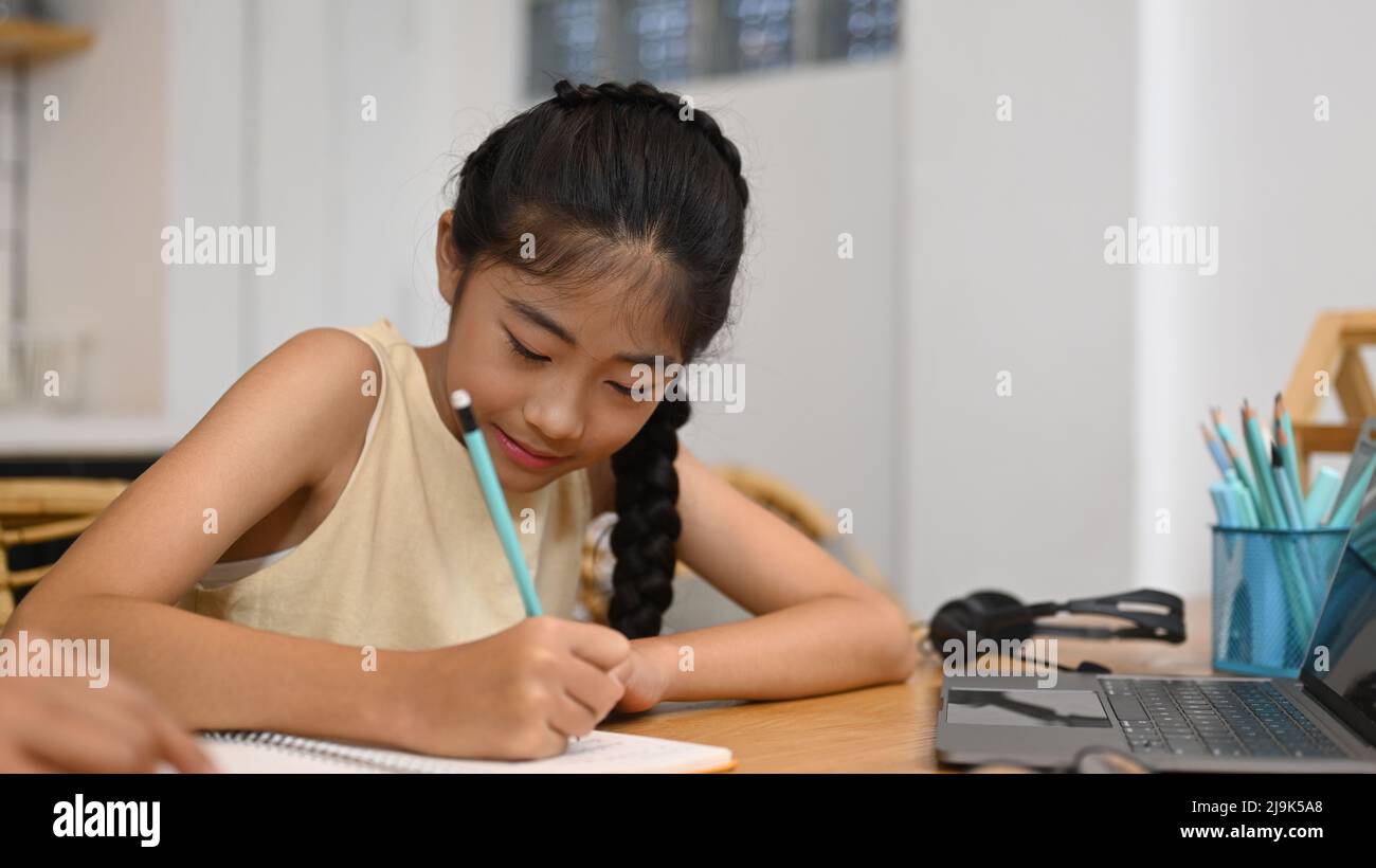 École asiatique fille d'apprentissage à distance en ligne, faisant des devoirs tout en étant assis à la table de cuisine Banque D'Images