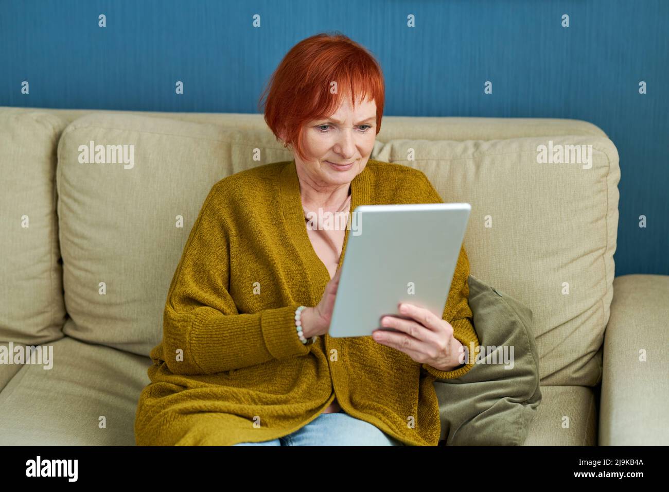 Portrait d'une femme mûre souriante utilisant une tablette numérique sur un canapé à la maison Banque D'Images
