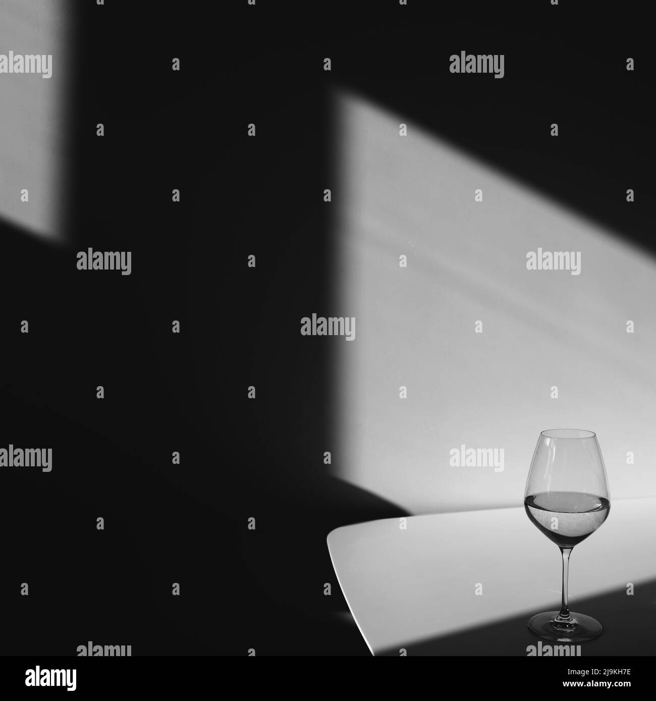 Un verre de vin blanc sur fond blanc avec une ombre. Chiaroscuro de la fenêtre. Photo en noir et blanc Banque D'Images
