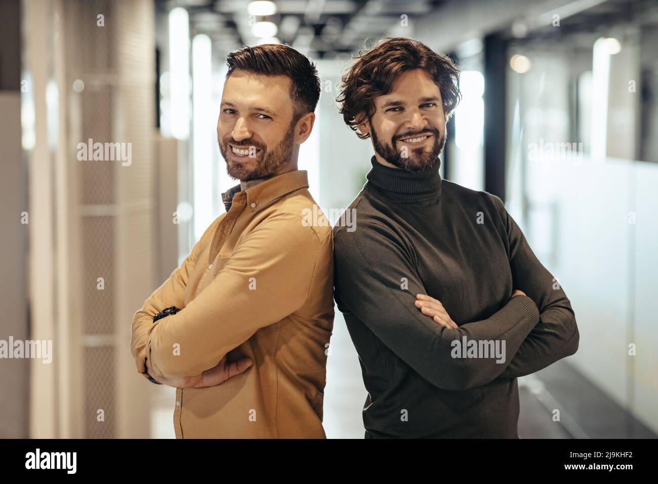Portrait de deux hommes d'affaires heureux debout avec des bras croisés, souriant à la caméra dans le hall d'entreprise moderne Banque D'Images