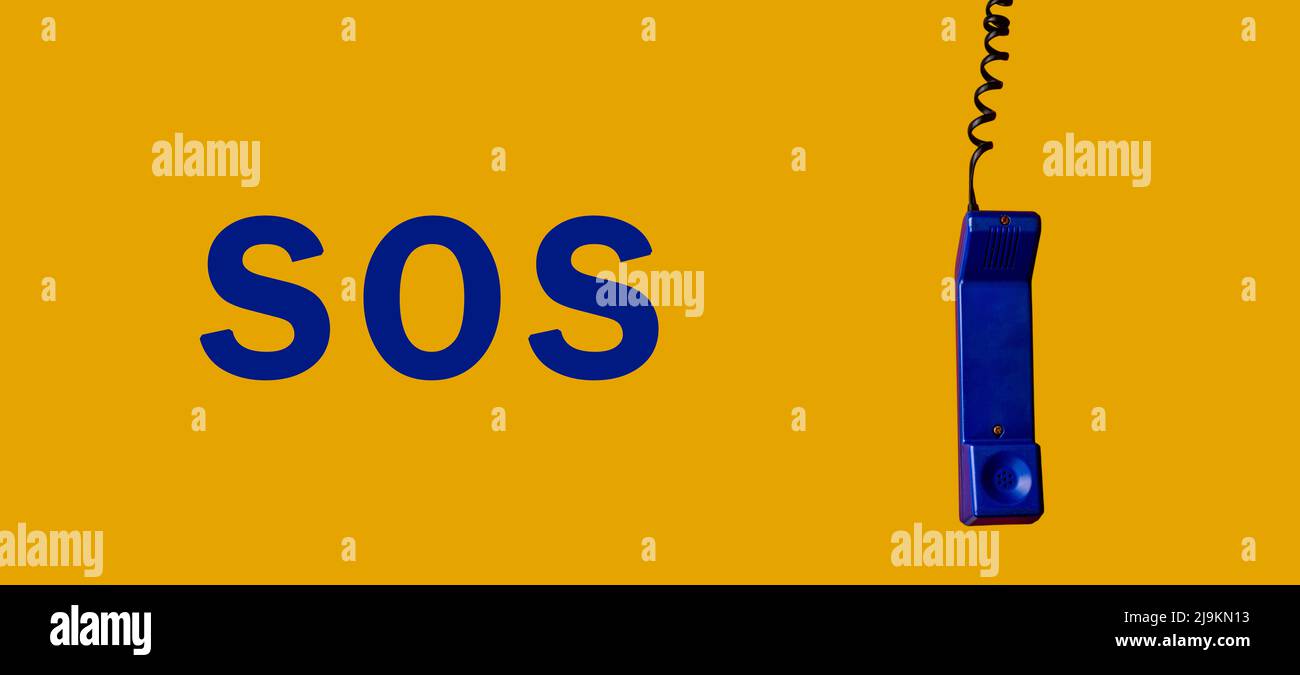 Vieux téléphone bleu suspendu d'un côté, sur fond jaune avec le mot SOS en bleu de l'autre côté, photographie panoramique. Banque D'Images