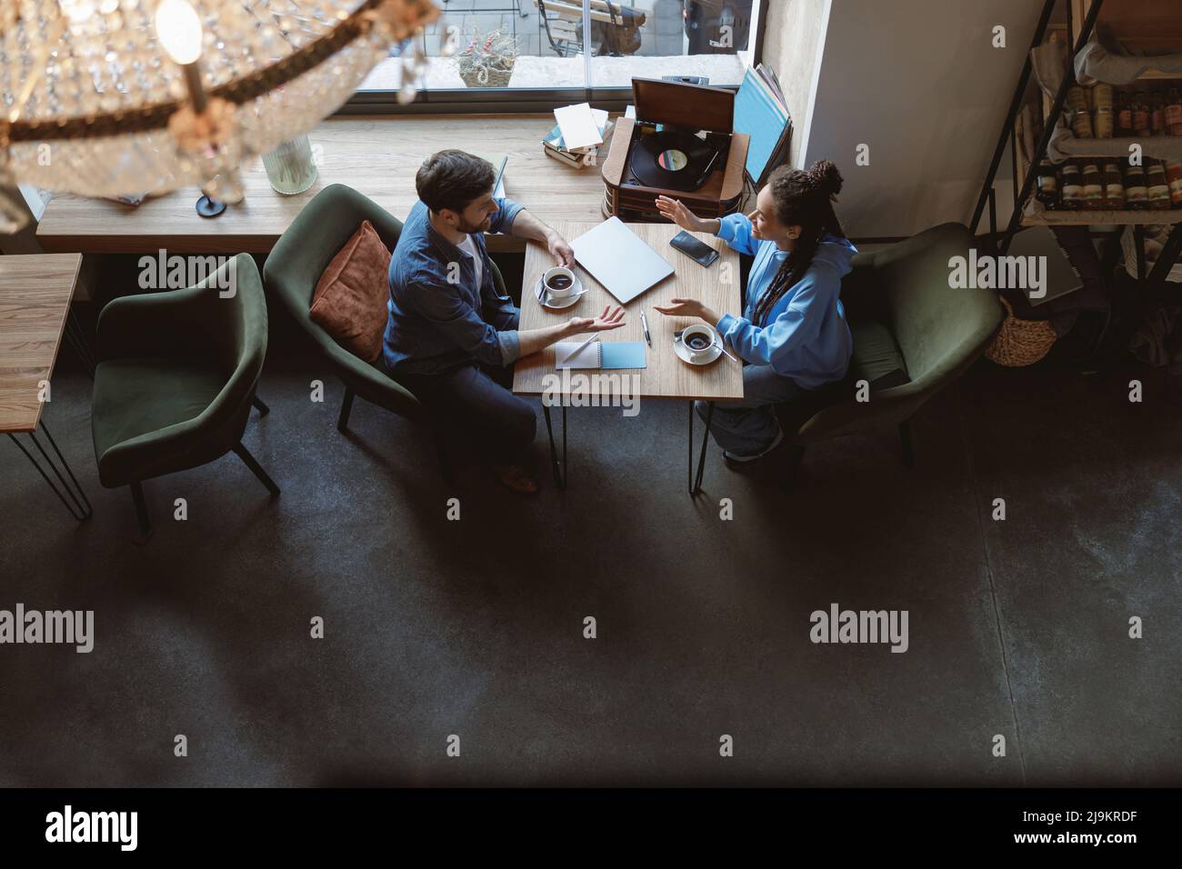 Vue d'en haut sur les courses mixtes de jeunes amis ou collègues qui parlent à table avec un café dans le café. Banque D'Images