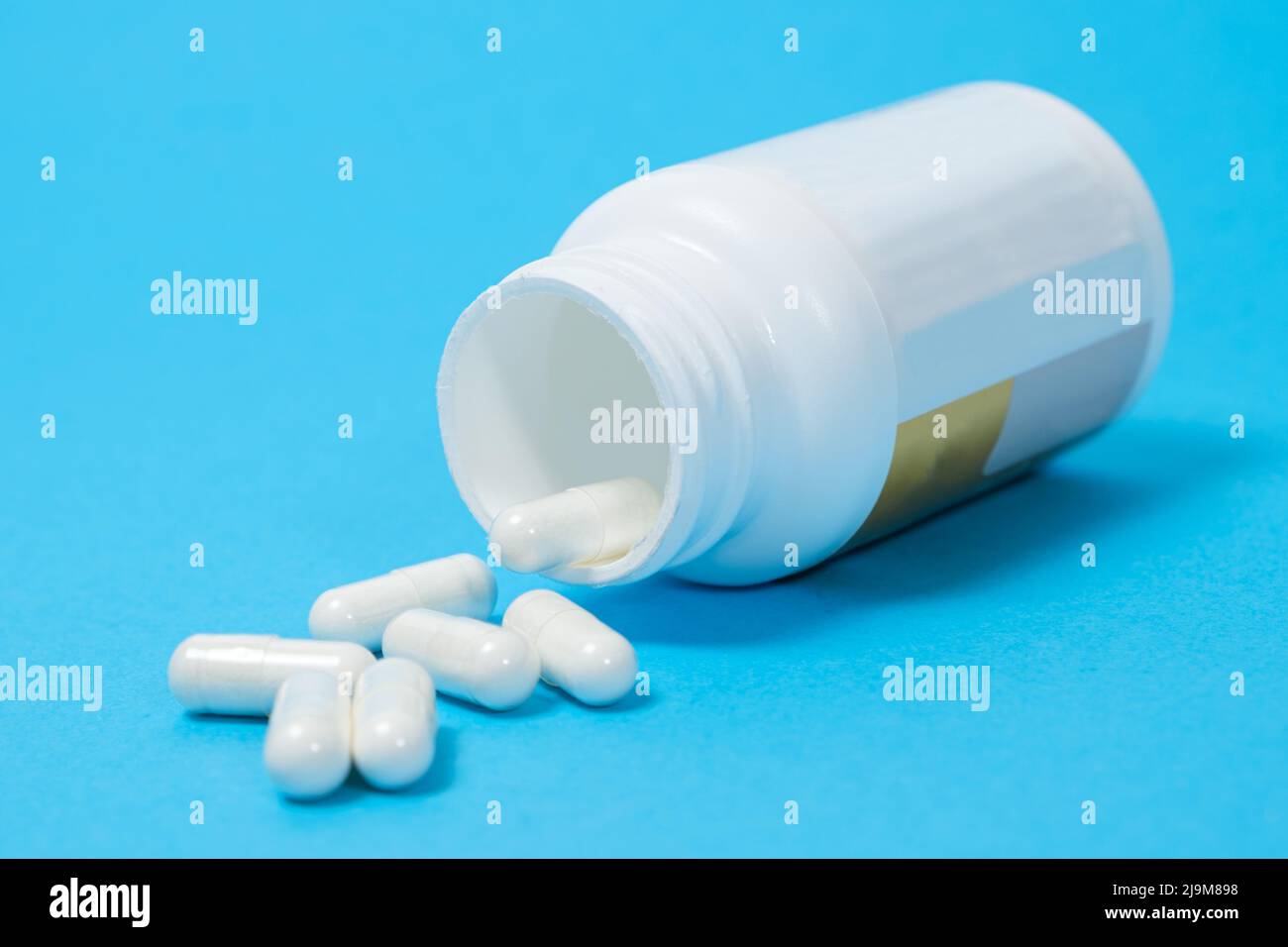 Un pot de compléments alimentaires et de capsules blanches sur fond bleu. Vitamines et oligo-éléments pour une alimentation complète Banque D'Images