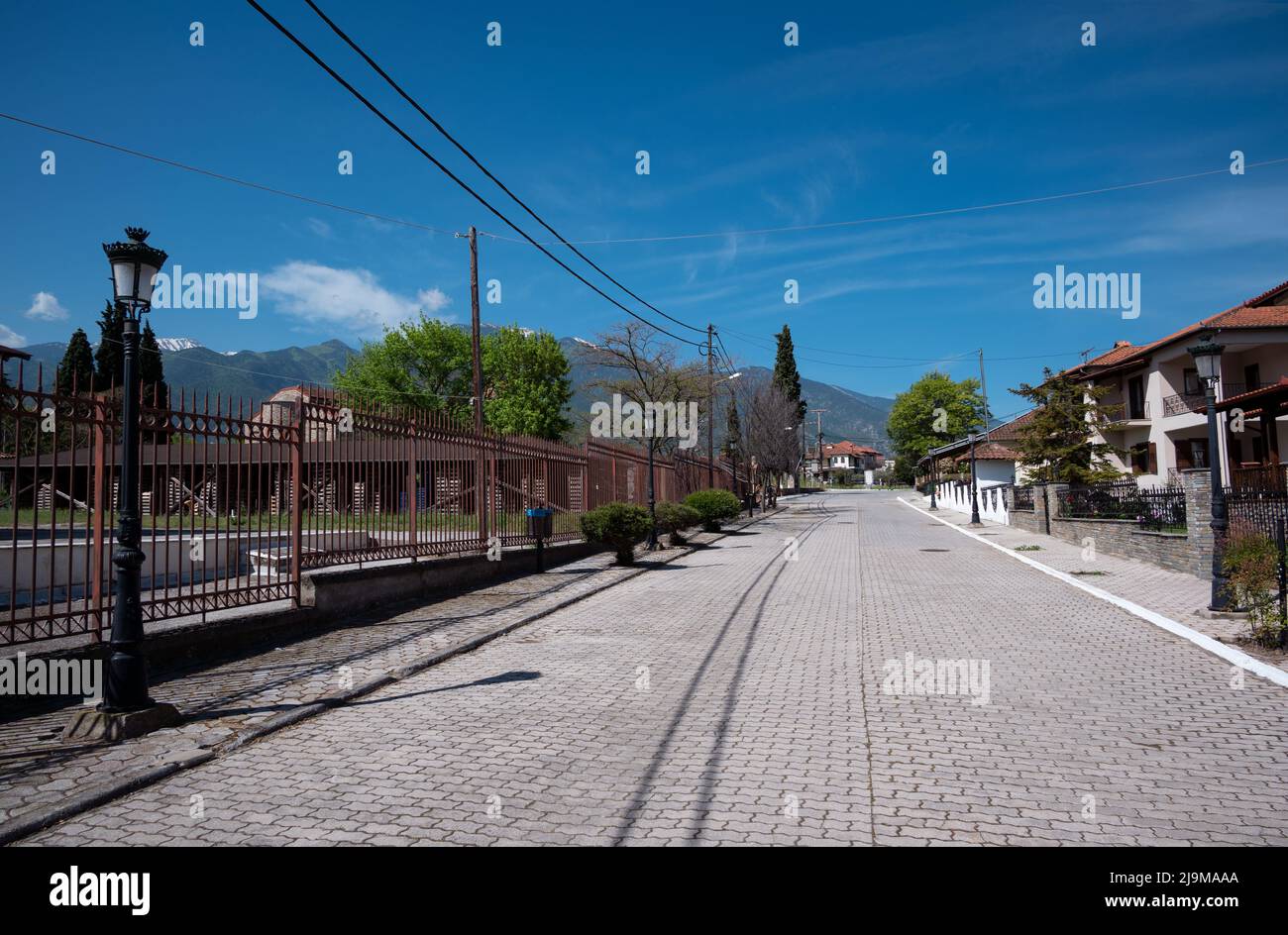 Vue pittoresque d'une rue avec des arbres verts, maisons de campagne, entouré de montagnes alpines et ciel bleu clair capturé à Dion Grèce. Banque D'Images