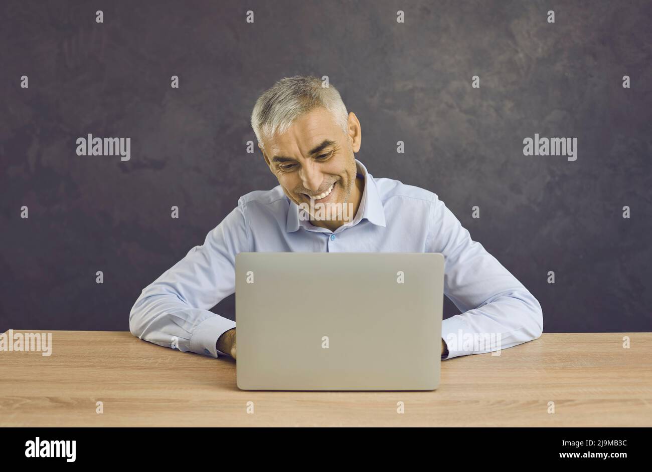 Un homme d'âge moyen souriant travaille sur le clavier d'un ordinateur portable Banque D'Images