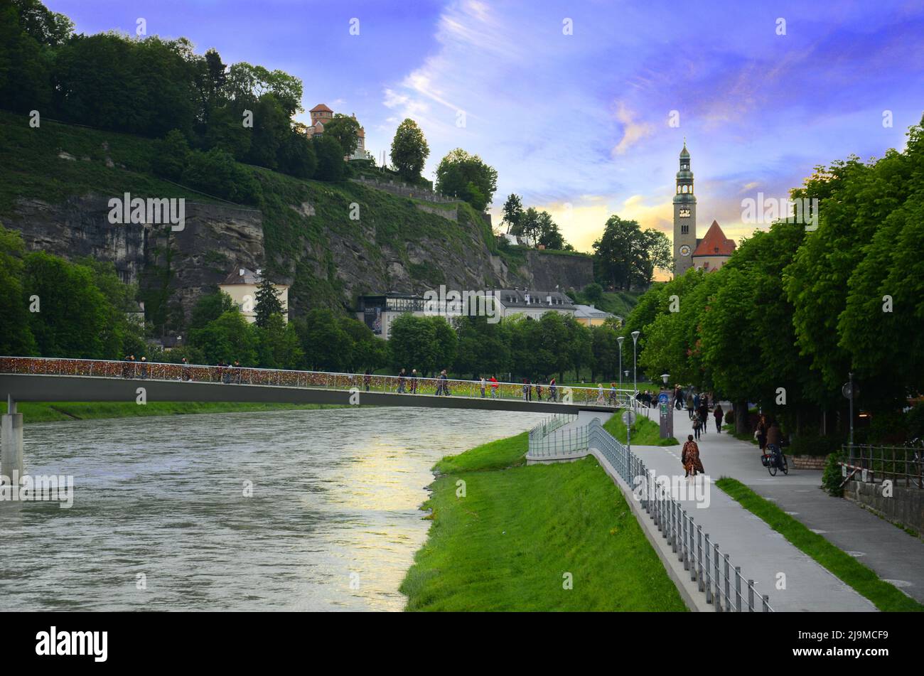 Belle vue sur l'église Leprosenhauskirche et le pont Mullner Steg au coucher du soleil avec le ciel violet et les touristes à Salzbourg, Autriche. Banque D'Images